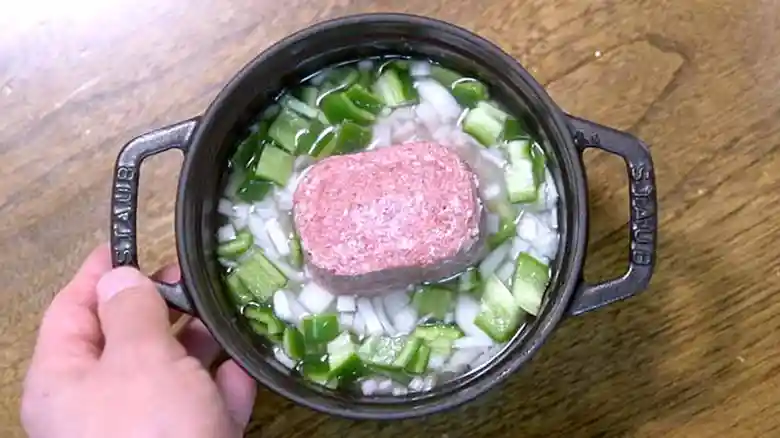 鍋にコンビーフを入れた写真です。米とピーマン、玉ねぎが入った鍋の中央にコンビーフがと置かれています。