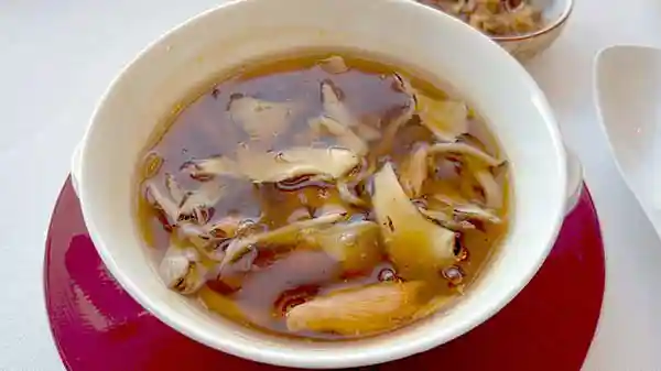 「五種のきのこと干し貝柱 鮑の細切りスープ」の写真です。とろみがかった茶色いスープの中に5種のきのこが浮かんでいます。