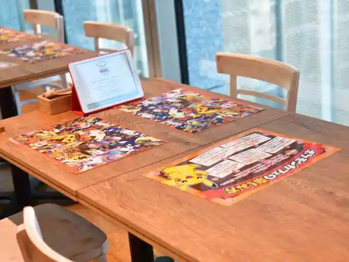 ポケモンカフェのテーブルの写真です。注文に使用するタブレトと、ハロウィンバージョンのランチマット、ポケモンカフェの楽しみ方を説明したシートが置かれています。