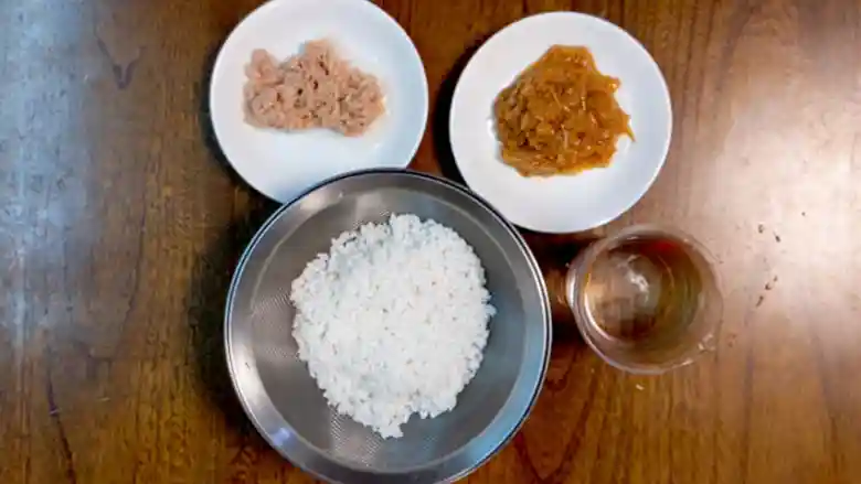 「なめ茸ツナ缶の簡単釜飯」の材料の写真です。白き小皿にツナとなめ茸が入っています。浸水した米はザルに入っています。
