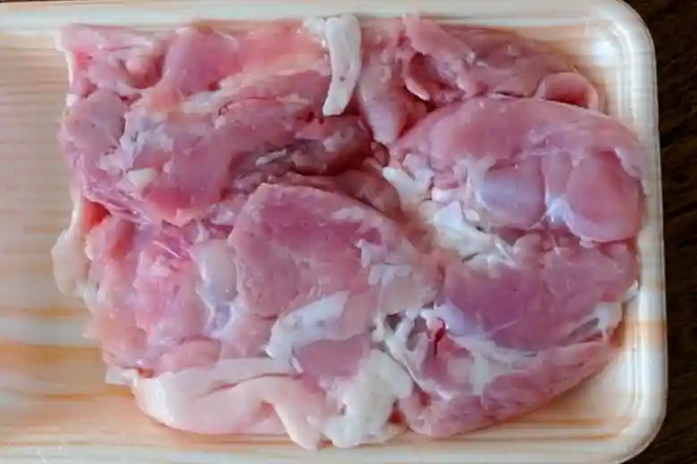 パックに入った鶏もも肉の写真です。パックは薄いオレンジ色で、発泡スチレンで作られています。