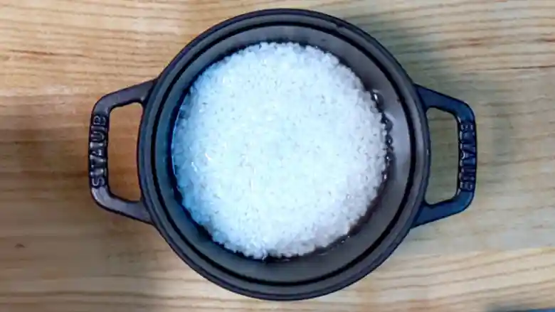 黒い鍋に入った米の写真です。鍋の直径は14cm、米の量は1合です。米は2時間浸水させてあります。