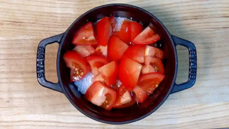 黒い鍋に米とトマトを入れた写真です。米の上に、鍋いっぱいにトマトを敷き詰められています。