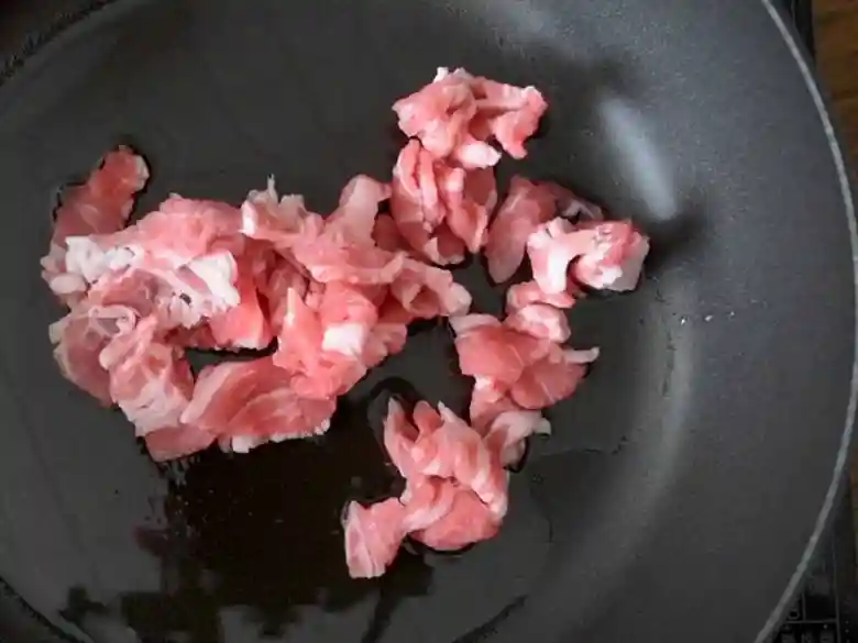 黒いフライパンで豚肉を炒めている写真です。
