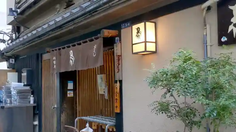 東京の京橋１丁目にある鶏料理店『伊勢廣京橋本店』の入り口の写真です。年季の入った日本家屋です。玄関には薄茶色の暖簾がかかっています。暖簾には伊勢廣のロゴマークである鳥の絵が白色で描かれています。