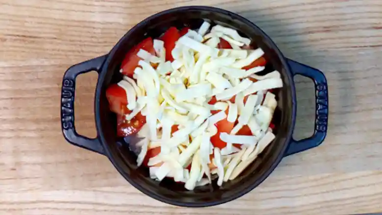 米とトマトが入った黒い鍋に、チーズを加えた写真です。チーズはピザ用で、幅5mm、長さ15mmほどに刻まれています。