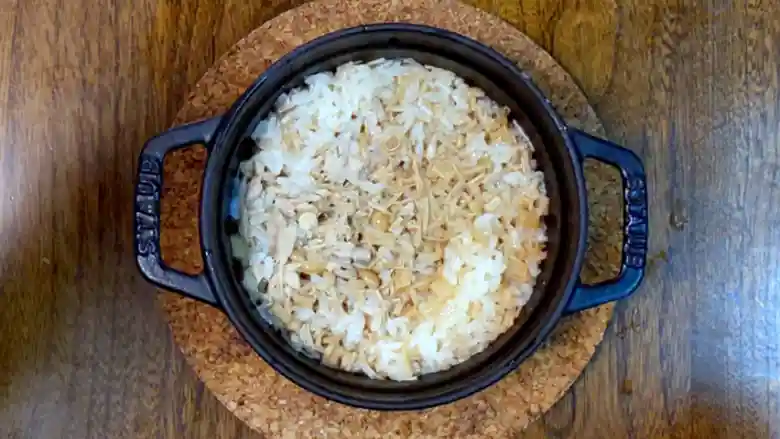 鍋のフタを開けた写真です。お米が薄い茶色に染まっています。表面になめ茸とツナが見えます。