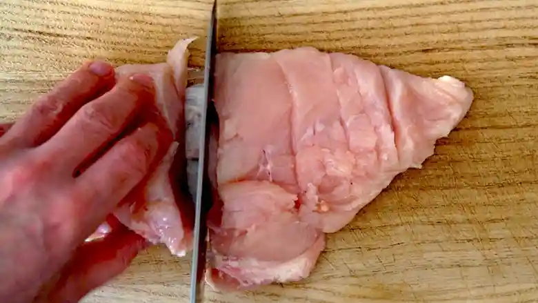 鶏むね肉を半分に切っている写真です。筋を切り離し、皮の脂はそぎ取ってあります。