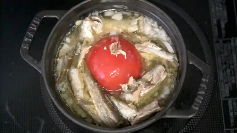 米とコンソメスープ、トマト、玉ねぎ、オイルサーディンが入った鍋の写真です。オイルサーディンの油で具材が輝いて見えます。