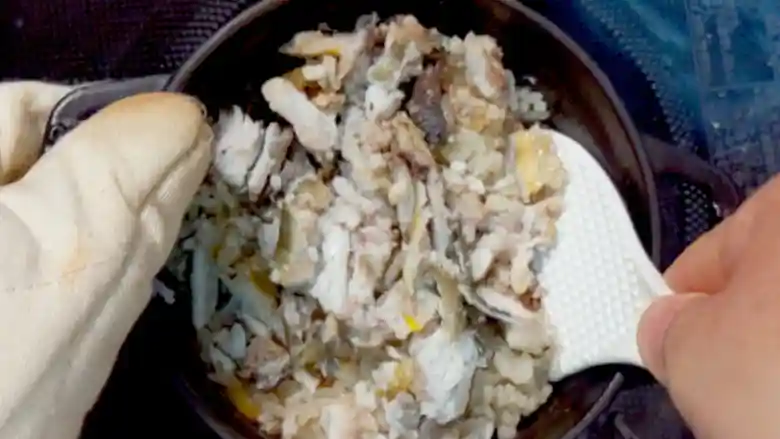 鍋の中でご飯と鮎を混ぜ合わせている写真です。しゃもじで混ぜています。