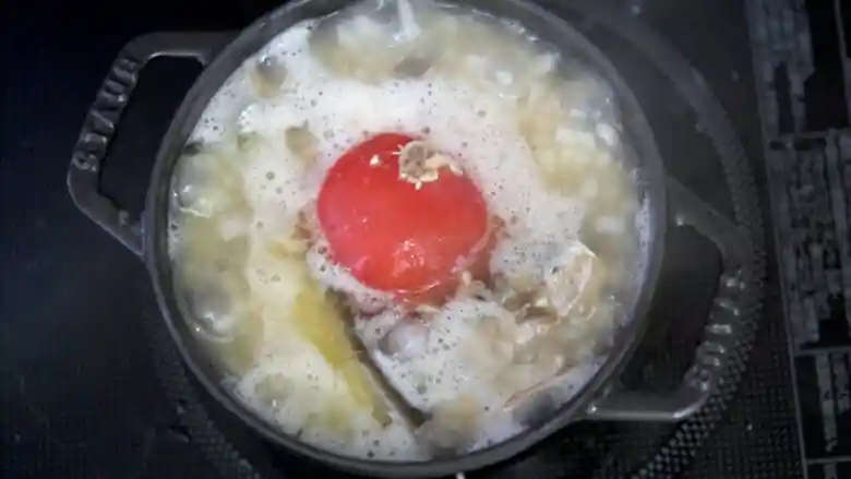 鍋の蓋を外した写真です。お湯が吹き上がって鍋からあふれそうです。真ん中に丸ごとのトマトが見えます。