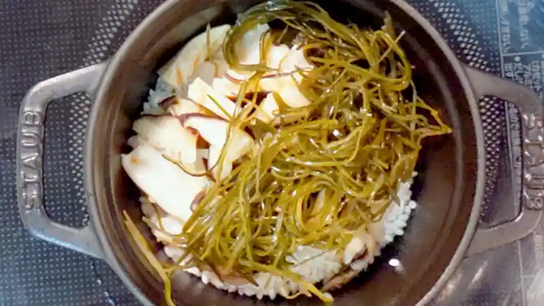 椎茸と切り昆布を鍋に加えた写真です。お米の上に北寄貝、その上に椎茸と切り昆布が重なっています。
