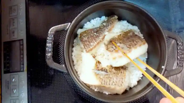 STAUB（ストウブ）鍋に入れた米の上に、焼いた鯛の切り身を並べた写真です。鍋は直径は14cmで黒い色をしています。