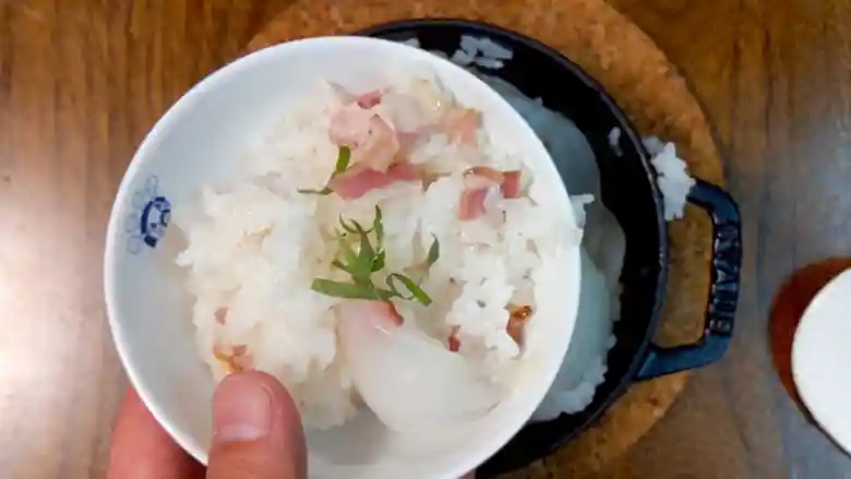 お茶碗によそった「新玉ねぎの炊き込みご飯」の写真です。大葉の緑とベーコンの赤、玉ねぎの水々しい白さがとても美しいです。