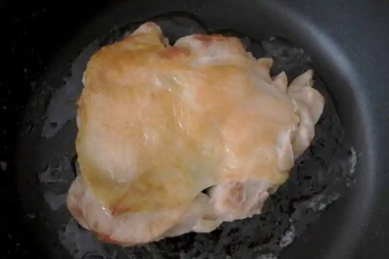 鶏もも肉を皮側を上にして黒いフライパンで焼いている写真です。もも肉の皮はパリパリに焼けて薄い茶色になっています。