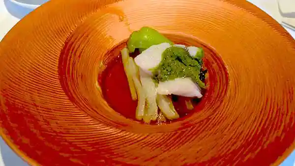 大紋ハタの葱生姜蒸しの写真です。直径30cm程の朱色の皿に白身の大紋ハタと青梗菜が盛られています。その上にニラとネギ、コリアンダー、パクチーを使った緑色のソースがかかっています。