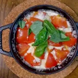 黒い鍋に入っている炊きあがった「マルゲリータ釜飯」の写真です。中央にバジルが散らされています。鍋は黒色、ご飯は薄いオレンジ色、トマトは濃いオレンジ色、バジルは緑色で、とても色鮮やかです。