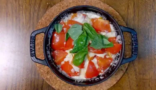 黒い鍋に入っている炊きあがった「マルゲリータ釜飯」の写真です。中央にバジルが散らされています。鍋は黒色、ご飯は薄いオレンジ色、トマトは濃いオレンジ色、バジルは緑色で、とても色鮮やかです。
