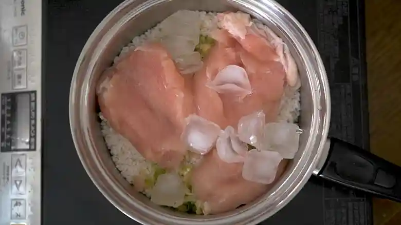 ご飯と鶏肉がはいった鍋に氷を加えた写真です。氷を加えることで温度の急激な上昇を防ぎ、米の甘みが引き出されます。

