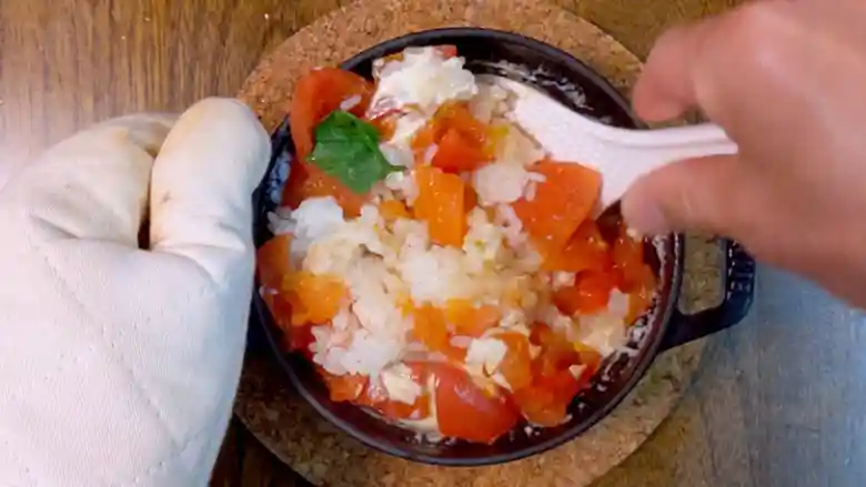 炊きあがった「マルゲリータ釜飯」を、鍋の中でしゃもじを使ってかき回している写真です。少しずつトマトの形が崩れています。