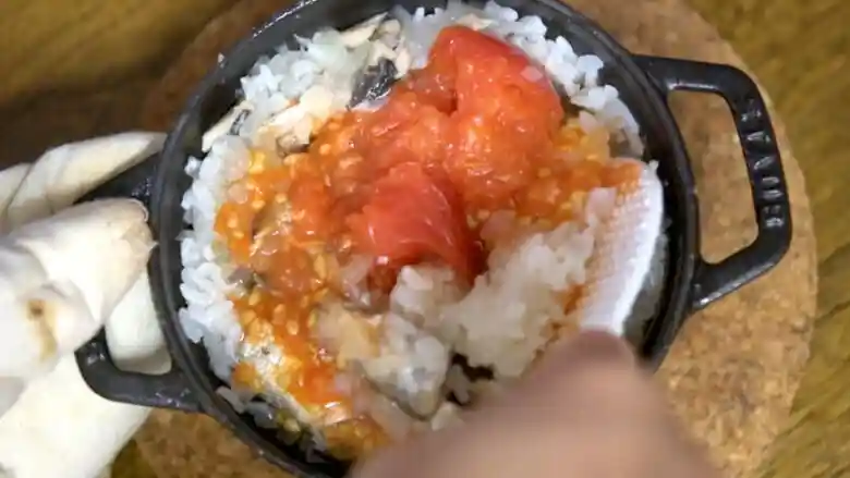 炊きあがった「オイルサーディンのイタリアン釜飯」をしゃもじでかき混ぜている写真です。トマトからたくさんの汁が出ています。白いご飯と赤いトマトの色合わせが鮮やかです。