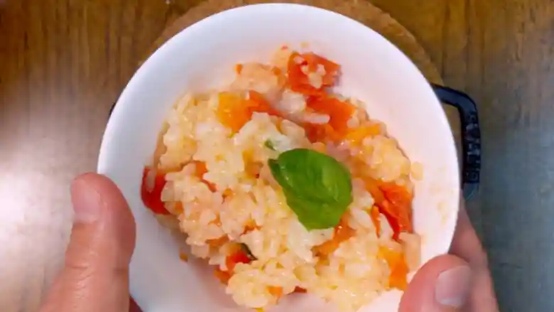 お茶碗にもった「マルゲリータ釜飯」の写真です。器は白色、ご飯は薄いオレンジ色、トマトは濃いオレンジ色、バジルは緑色で、とても色鮮やかです。