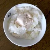 お茶碗によそった海南チキンライス釜飯の写真です。ご飯の上に大きな鶏肉がのっています。