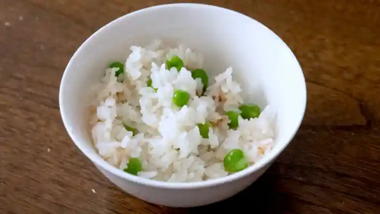 白色のお茶碗によそった豆ご飯の写真です。ご飯の一部はお焦げになっています。