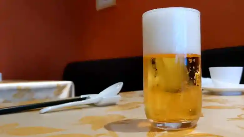 グラスにはいった生ビールの写真です。テーブルクロスは薄茶色で、木の葉が描かれています。