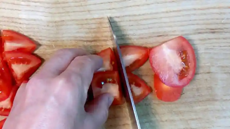 まな板の上でトマトを切っている写真です。切ったトマトの大きさは一口大です。
