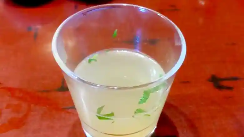 鶏スープの写真です。透明なガラスの器に入っています。スープは淡黄色で、刻んだ緑色のネギが浮かんでいます。