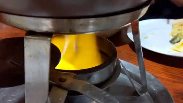 チーズフォンデュの鍋を温めているコンロの写真です。オレンジ色の炎が鍋底を温めています。