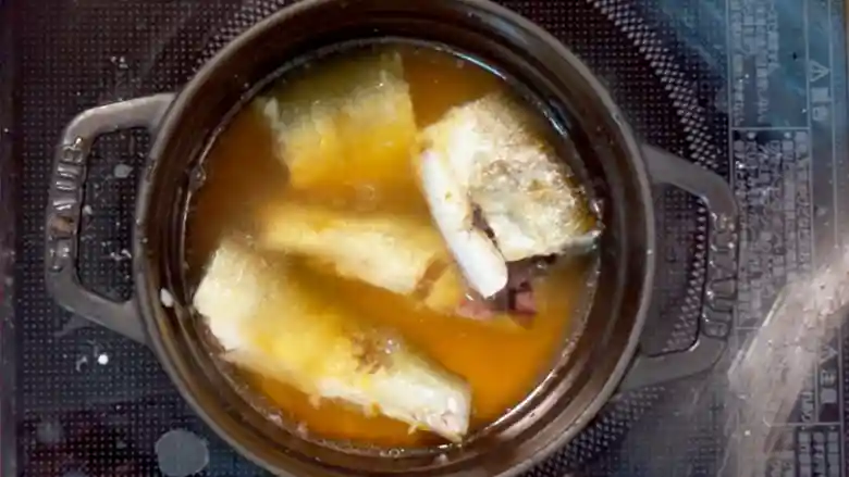 鍋にお米とだし汁、鮎を入れた写真です。鮎は胴で切断されています。だし汁は昆布ダシです。醤油を加えたので薄い茶色です。