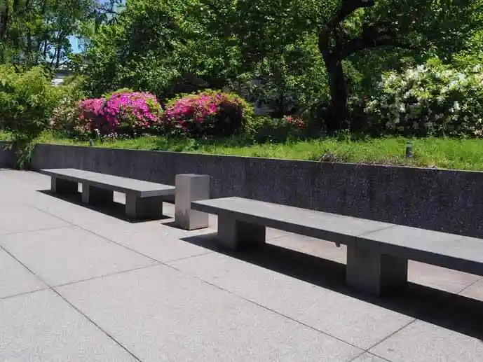 法隆寺宝物館の前にあるベンチの写真です。石製のベンチが2脚並び、背後に赤い花が咲いています。