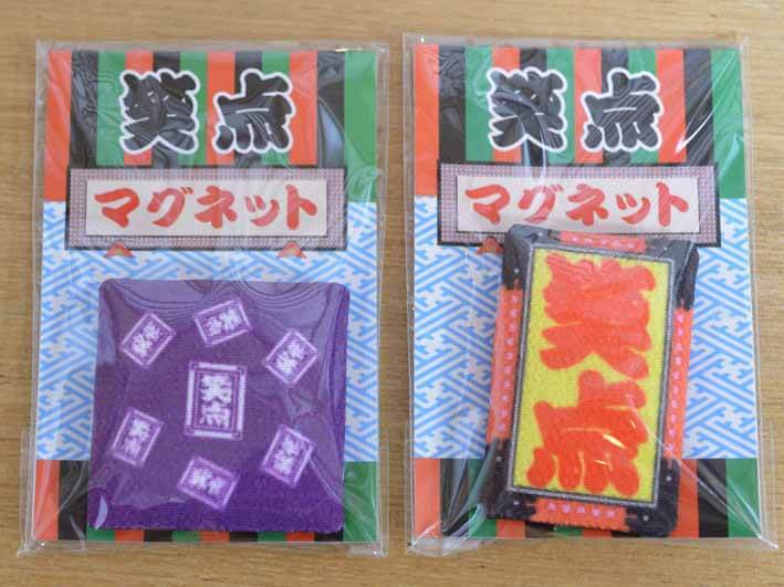 会場に設置された「笑点商店」という笑点グッズの販売コーナーで購入した笑点マグネットの写真です。右側は笑点の紫色の座布団、左側は笑点の舞台看板がマグネットになっています。看板にはオレンジ色の文字で「笑点」と縦書きで書かれています。看板の背景は黄色です。大きさは両方とも10cmほどの高さです。