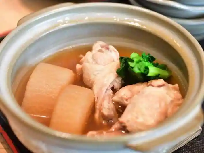 骨付き鶏と大根の煮物の写真です。陶器の小鍋に鶏と大根が二切れ入っています。