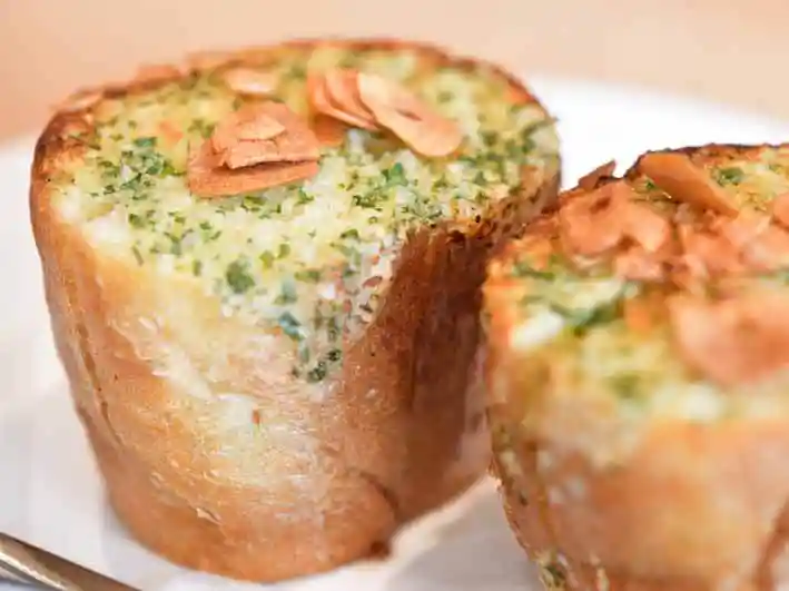 ガーリックトーストの写真です。パンにバターがたっぷりしみ込んでいます。パンの表面にはスライスした焦がしにんにくがのっています。
