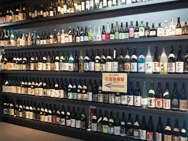 吉池食堂の壁に並んだ酒ビンの写真です。横幅4m、高さ2m5段の棚一杯に酒ビンが並べられています。