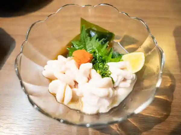 真鱈の白子ポン酢の写真です。ガラスの鉢に、白子と大葉、わけぎ、昆布、すだち、もみじおろしが添えられています。