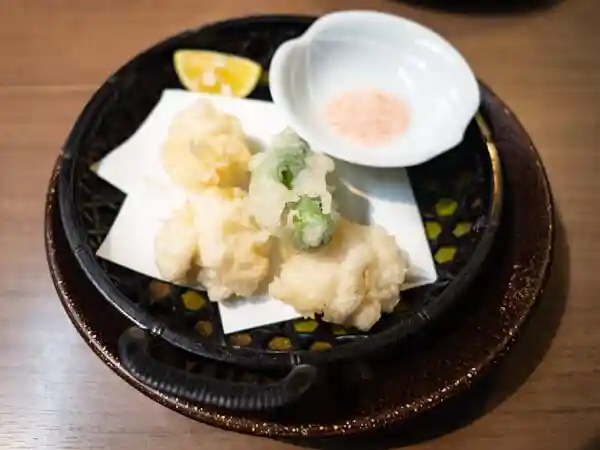 真鱈の白子天ぷらの写真です。すだちとししとうが添えられています。梅塩をつけて食べます。