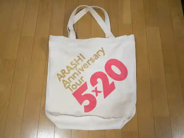 コンサート限定のショッピングバッグの写真です。大きめのトートバッグで、赤文字「で5×20」、金色の文字で「ARASHI Tour」と書かれています。コンサートグッズをこのバッグに詰め込みます。コンサート当日はこのバッグを持った大勢のファンを電車の中で見かけました。