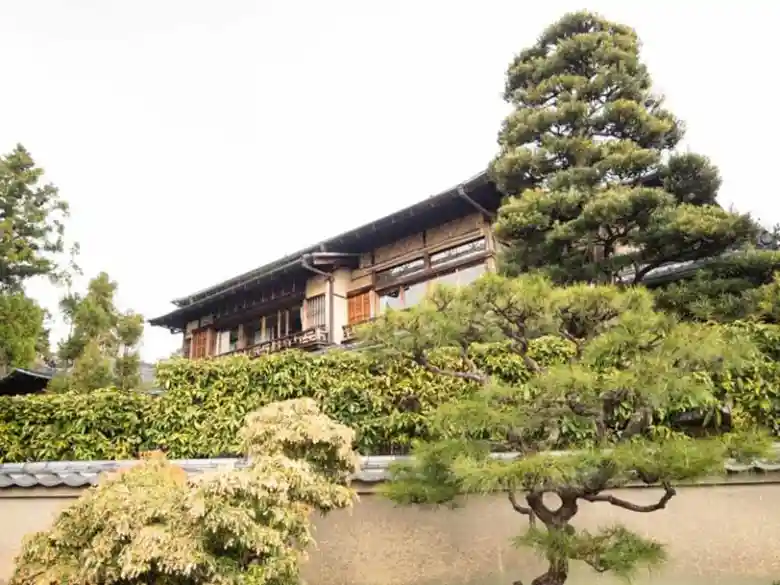 吉田山荘を塀の外から撮影した写真です。2階建ての木造建築です。庭には大きな松の木が植わっています。