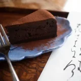 注文したチョコレートケーキの写真です。この葉の形をした青色の皿に盛られています。皿の脇には女将が筆でしたためた和歌の短冊がそえられています。