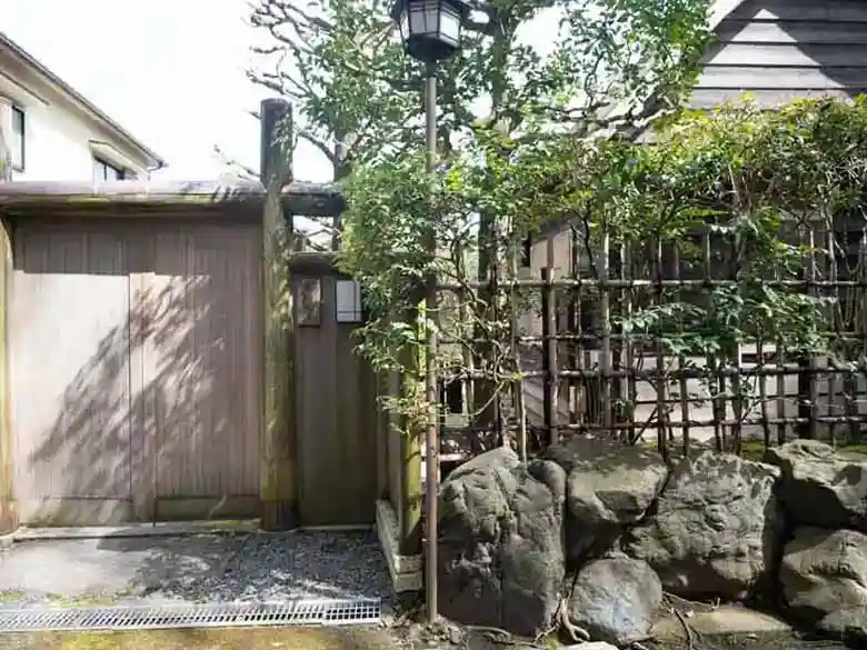 石村亭の入り口の写真です。「石村亭」と書かれた表札がかかってる門と垣根が写っています。建物や庭の様子は外から見えません。