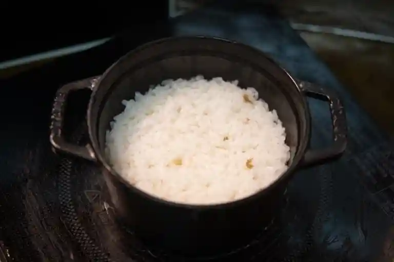 黒い鍋でご飯を炊き上げた写真です。直径14cm、高さ10cmの黒い鍋に炊きあがったご飯が入っています。