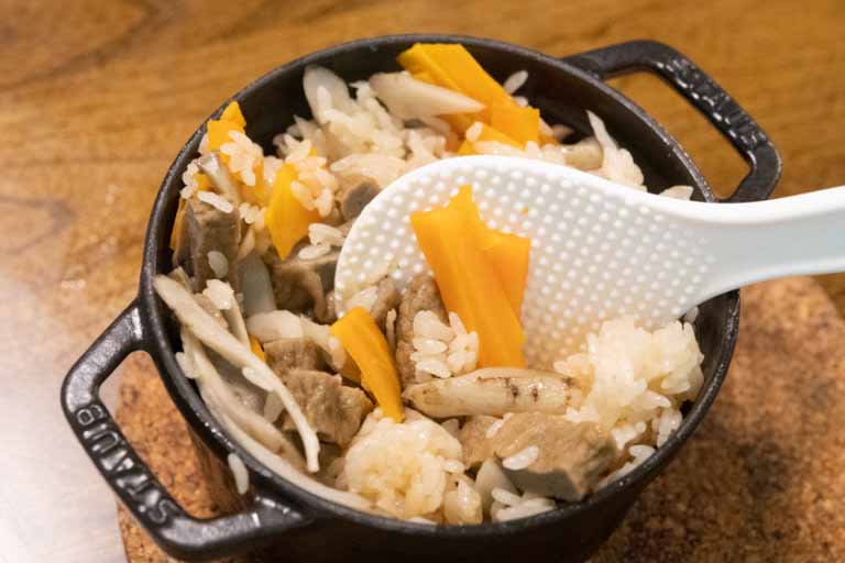 炊き上がった「じゃこ天釜飯」を白いしゃもじでかき混ぜている写真です。ご飯は薄い茶色に染まっています。 