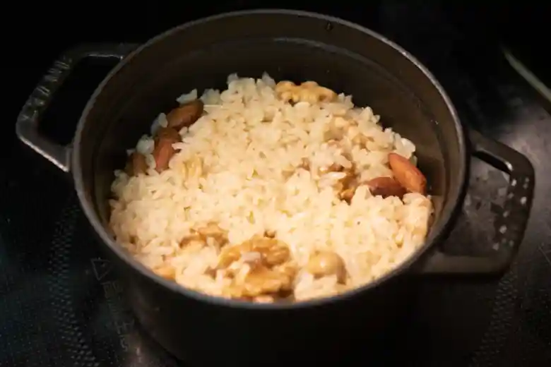 鍋に米とミックスナッツ、水を入れた写真です。表面にオリーブオイルが浮いて、光って見えます。