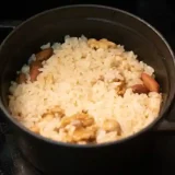 炊き上がったミックスナッツ釜めしの写真です。鍋の蓋を取って写しました。薄い茶色に染まったご飯にナッツが混じって見えます。