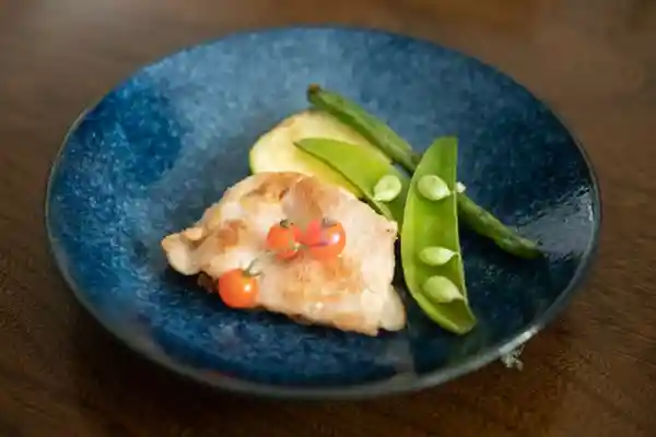 青い皿にとりわけた「塩麹味噌豚と焼き野菜」の写真です。塩麹味噌豚にはかすかに焦げ目がついています。野菜はインゲンとズッキーニ、ミニトマトがそえられています