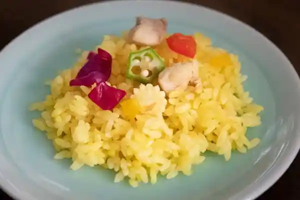 薄い水色の皿によそった「夏野菜と鶏肉のピラフ」の写真です。ご飯はサフランで黄色く染まっています。
